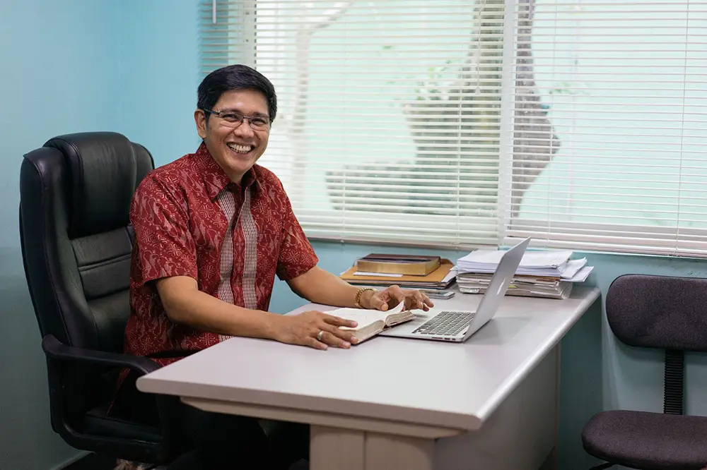 Rico Villanueva sitting at a desk reading his Bible and laptop